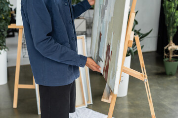 Cropped view of african american artist taking painting from easel in studio.