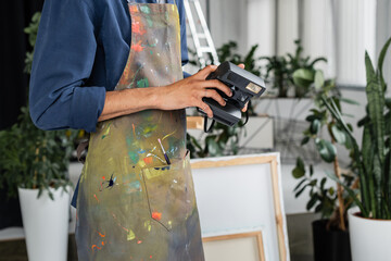 Cropped view of african american artist in apron holding vintage camera in workshop.