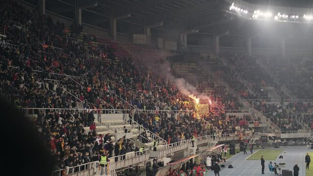 Football, soccer supporter fans in full stadium celebrate a goal with burning fire torch in open air roof stadium at night, slow motion
