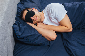 Top view of a young man wearing a sleep mask resting in his bedroom. Relaxation, rest after work.