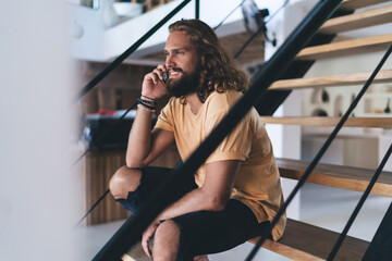 Cheerful man talking on smartphone while sitting on stairs