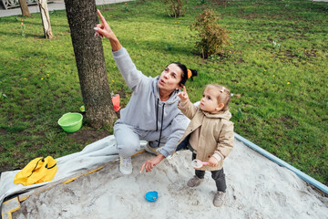 Benefits of Sand Play. Sandpit play ideas to get kids learning while having fun. Senior woman grandmother and little toddler girl granddaughter together playing in sandbox in spring garden