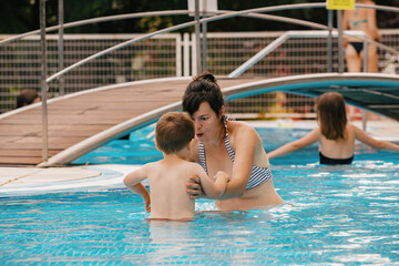 Mom teaches a little boy to swim in the pool.
