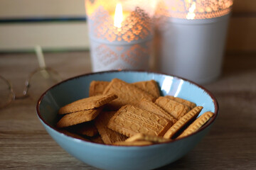Glasses, bowl of biscuits, lit candles and books in the background. Selective focus.