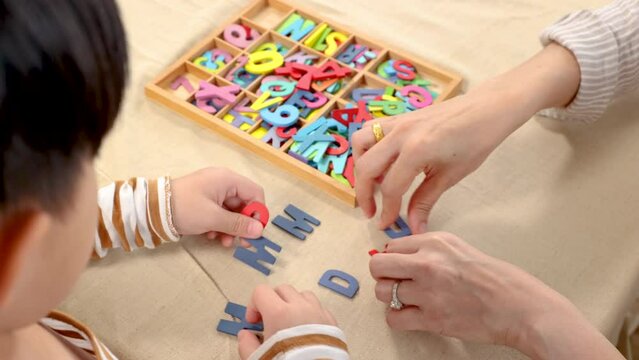 Asian happy single mother and son playing alphabet games with plastic toys, mom helping child learn foreign language for improve mental health and memory. family spending time together in holiday.
