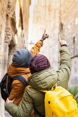 People on vacation on their backs in winter clothes pointing at the Cathedral in the Gothic quarter of Barcelona (Spain), selective focus on the gray cap.