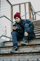 A young man sitting on outdoor staircase while using mobile phone. One man alone sitting on stairs...