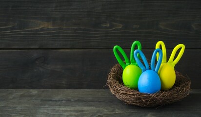 
Photo with funny Easter eggs on a wooden background.  Bunnies in the nest.  Front view background, copy space for text.  Concept creative eggs, crafts.

