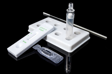 A coronavirus rapid test kit with a liquid vile and nasal swab in a tray on a black backdrop.