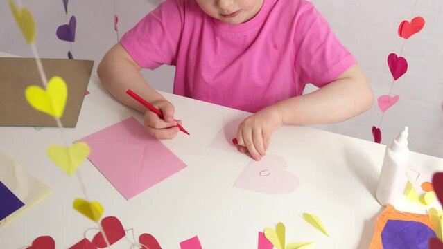 cute girl with blond curly hair signs a card in the shape of a heart