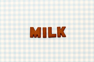 Word MILK made from chocolate cookies on blue checkered background. 