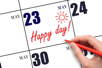 Hand writing the text HAPPY DAY and drawing the sun on the calendar date May 23