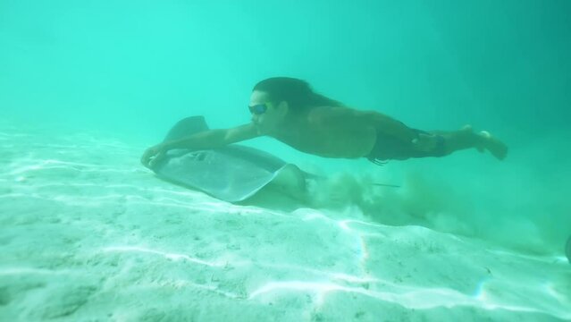 Underwater Tahiti. Traditional Polynesian man swims with sting ray. Bora Bora, French Polynesia. Exotic vacation activities, romantic getaway, honeymoon destination.