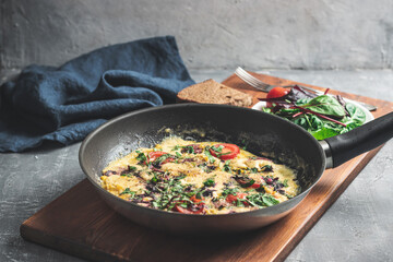 Cooked omelette with sausage, cheese, tomato and herbs in a pan, on wooden board