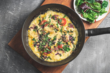 Cooked omelette with sausage, cheese, tomato and herbs in a pan, on wooden board, top view