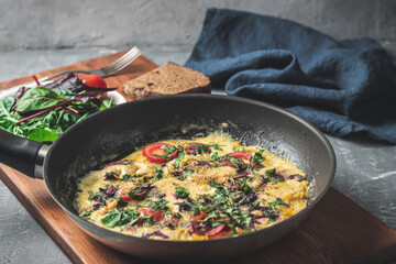 Cooked omelette with sausage, cheese, tomato and herbs in a pan, on wooden board
