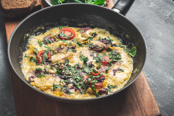 Cooked omelette with sausage, cheese, tomato and herbs in a pan, on wooden board