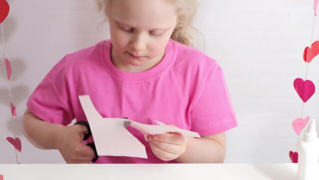 a girl cuts out a heart from colored paper sitting at a table, do-it-yourself greeting cards for valentine's day 4k