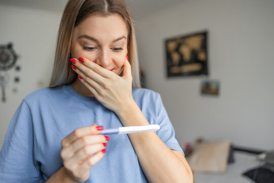 Happy Smiling Woman Looking At Pregnancy Test At Home. Pregnancy, Fertility, Maternity, Emotions And People Concept .