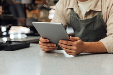 Close-up of hands holding a digital tablet. Unrecognizable bartender in an apron holding a portable...