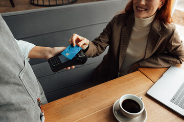 Unrecognizable waiter holding a card machine while a female customer paying by credit card for the...