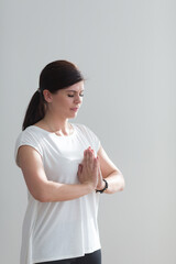 Obraz premium Attractive brunette girl in casual clothes prays for wellness of family, keeps palms pressed together in praying gesture, saying namaste. Human emotions, gesture concept. Mock up copy space