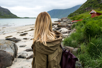 Woman with a backpack looks at the fjord. Ocean and mountain landscape. Scenic view. Travel, adventure. Sense of freedom, lifestyle. Lofoten Islands. Explore North Norway. Summer in Scandinavia