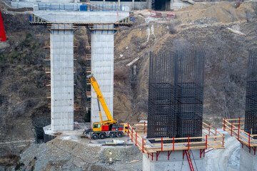 Process construction bridge for cars and road transport infrastructure in mountainous area. Two concrete piers for bridge with wooden scaffolding and metal frame are located next to cliff. - Powered by Adobe