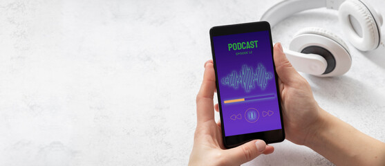 Closeup of woman hands who holding smartphone and listening podcast. White headphones on the white table. Empty space