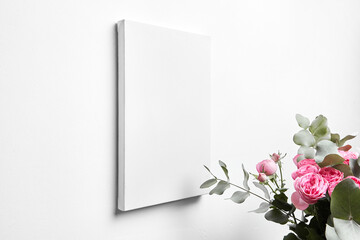 White canvas mockup hanging on white wall and bouquet of pink roses with eucalyptus leaves. Blank canvas, interior decor