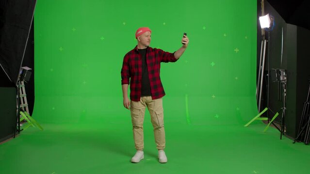 Full body video shot of man dressed casual clothes taking selfie on smartphone on green screen background, chroma key