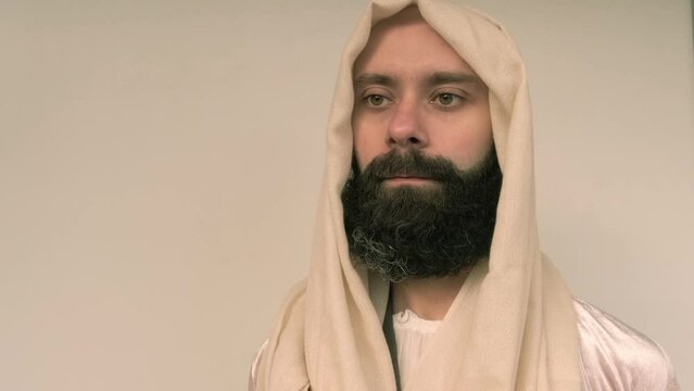 close-up male face in beige head cape, young pensive bearded man in image of Jesus Christ, satisfied guy with 30 years seriously looks away, concept Christian religion, holiday of Easter, Christmas