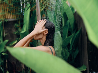 Woman takes a shower and washes her head and hair outdoors, closed eyes and smile on the background...