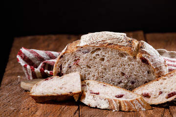 Sliced artisan crunchy sourdough bread with cranberries on a linen towel on a stone table, close-up.