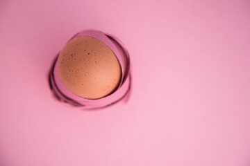 Happy Easter. Minimalist close-up of an egg wrapped in colored ribbons as if it were a nest. Isolated on pink background. Fragility and protection concept. Copy space