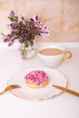
Coffee cup and sweet strawberry donut on golden plate with flower bouquet
