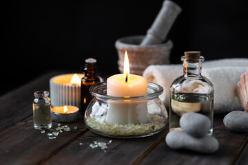 Fototapeta na wymiar Spa setting with essential oil, candle, sea salt, pebbles, towel on dark wooden background. Massage, aromatherapy. Natural organic ingredients for relaxation, detention. Wellness in salon concept