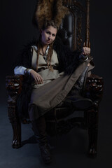 An authoritative, self-confident woman in a Viking-style fantasy costume, sitting on a high chair or throne. skirt with shirt and long fur cape, Scandinavian style