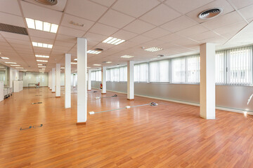 Large empty space with ceiling tiles, fluorescent lights, light brown laminate flooring and white...