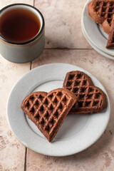 Heart form chocolate waffle cookies in white plate for Valentine's day with tea on pink tileba ckground. Sweet sweets with love. Gift for Valentine's Day