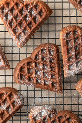 Heart form chocolate waffle cookies sprinkled with sugar powder on baking rack for Valentine's day close up, texture. Sweet sweets with love. Gift for Valentine's Day