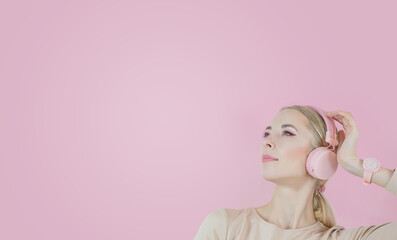 A girl listens to music in pink headphones on a pink background. The pleasure of listening to music Space for text on the right