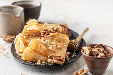 Crepes with honey or syrup and nuts Walnut on beige textured background close up. Pancake day or Maslenitsa traditional food concept