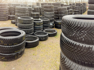 Used tires. Sale of used tires, stacks of different car tires lie on the ground. Buying used tires is a cheap alternative to new - obrazy, fototapety, plakaty