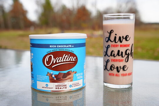 A canister of Nestlé Ovaltine rich chocolate milk mix and a glass of milk sit outside.