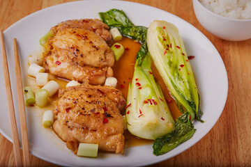 Chicken thighs in a sweet honey sauce with bak choy on a white plate with chopsticks.