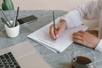 Close-up of a woman sitting at a desk writing a to do list