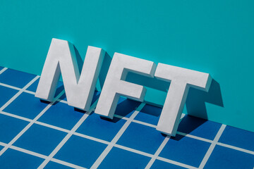 NFT letters and shadow on a blue background with a gridded pixel in cyberspace. Minimal concept of innovation of the future of transactions in the blockchain and virtual art. High quality photo