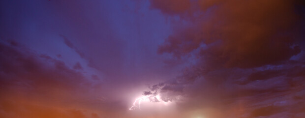 Naklejka na ściany i meble panoramic photograph of lightning in the center of a dark blue and orange cloudy sky