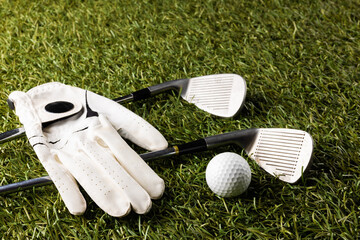 Close up of white glove, golf ball and golf clubs on grass with copy space